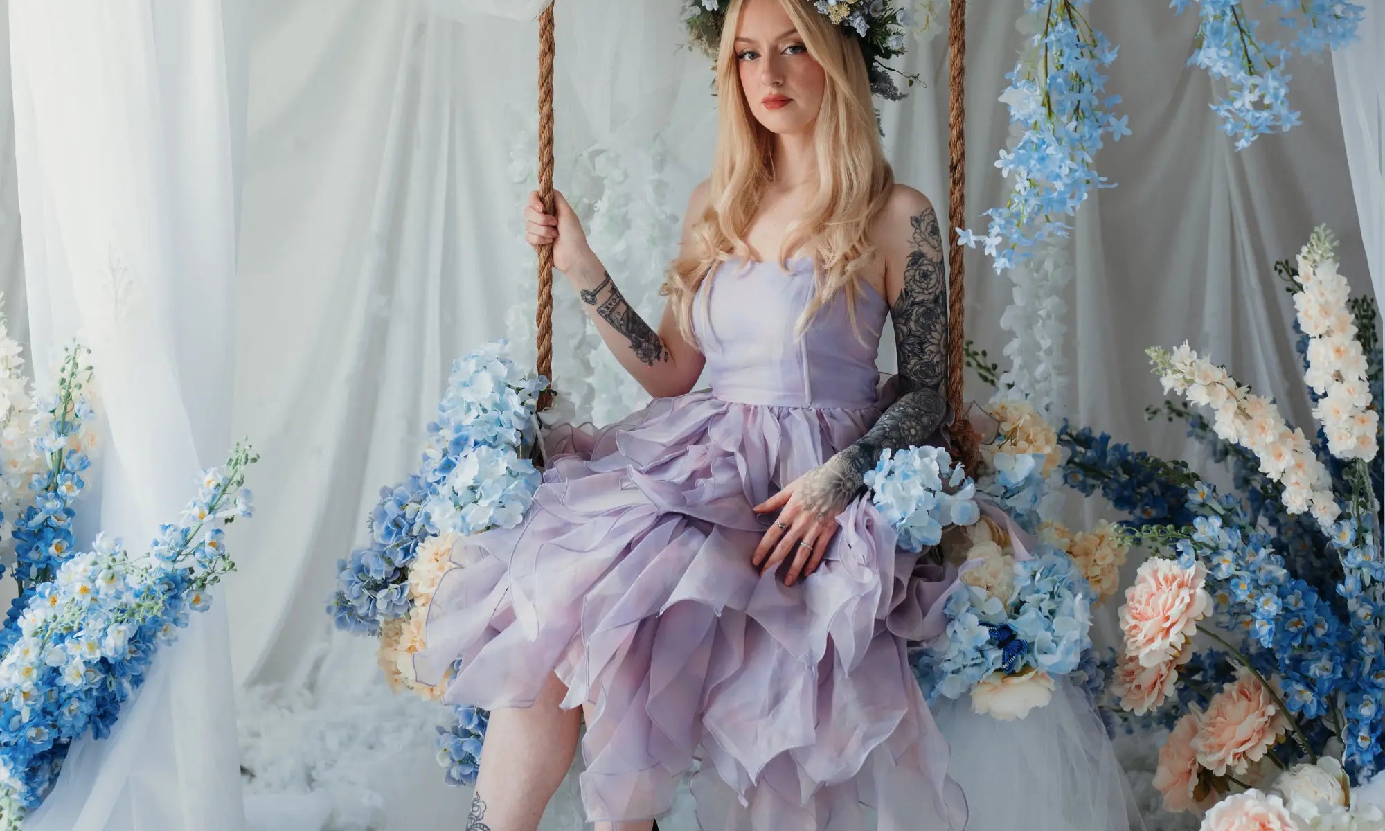 A woman sitting on a bench surrounded by florals wearing the Eventyr tulip dress.