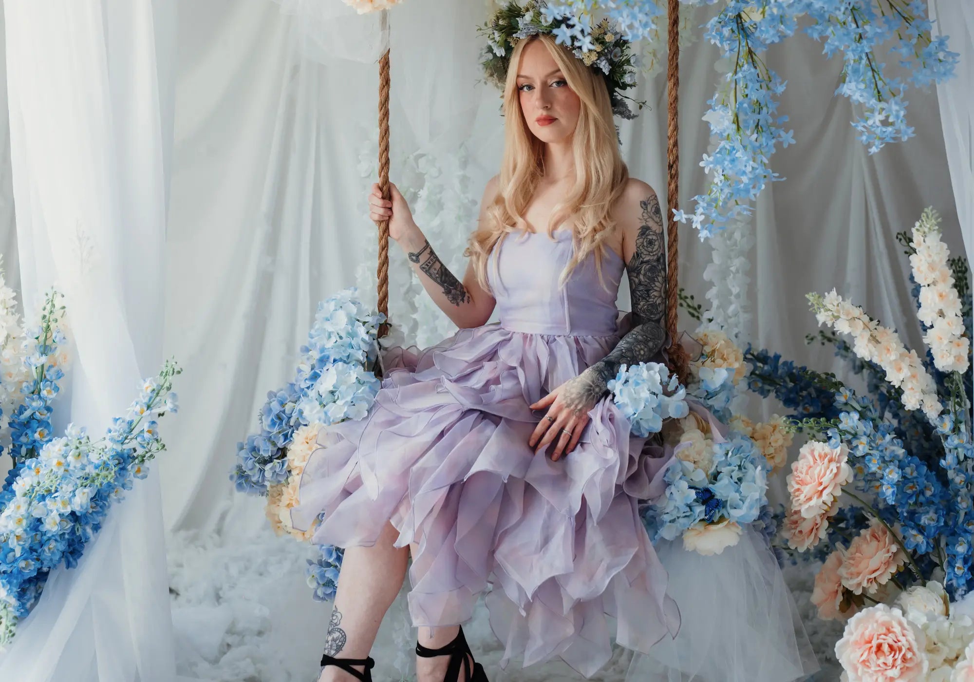 A woman sitting on a bench surrounded by florals wearing the Eventyr tulip dress.