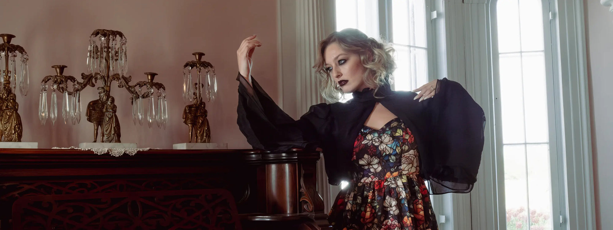 A woman wearing a stained glass printed mini dress, standing by a piano, showcasing the gothic fairytale collection.