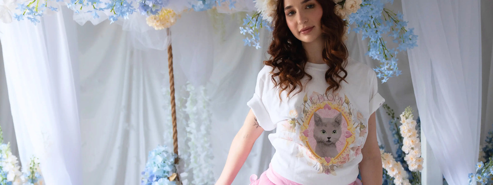 Woman wearing floral crown and cat graphic tee in dreamy garden setting.