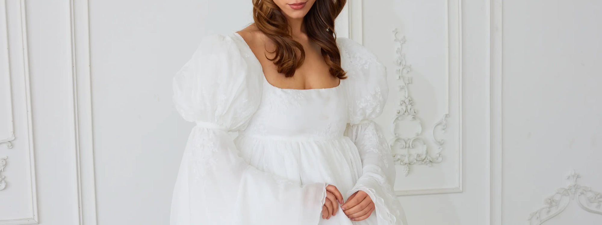 A woman wearing the Ivory Fairy bridal mini dress and a giant white bow belt. With ornate walls in the background.