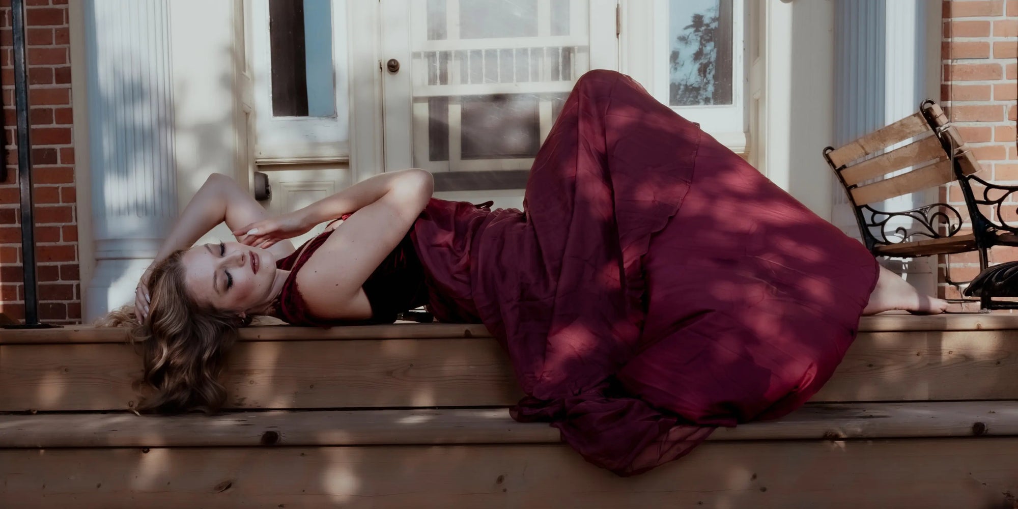 A woman lying down on wooden steps wearing a red corset maxi dress.