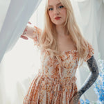 Model in Twilight Bloom Meadow Gown posing by window, emphasizing ruffled neckline and fitted waist.