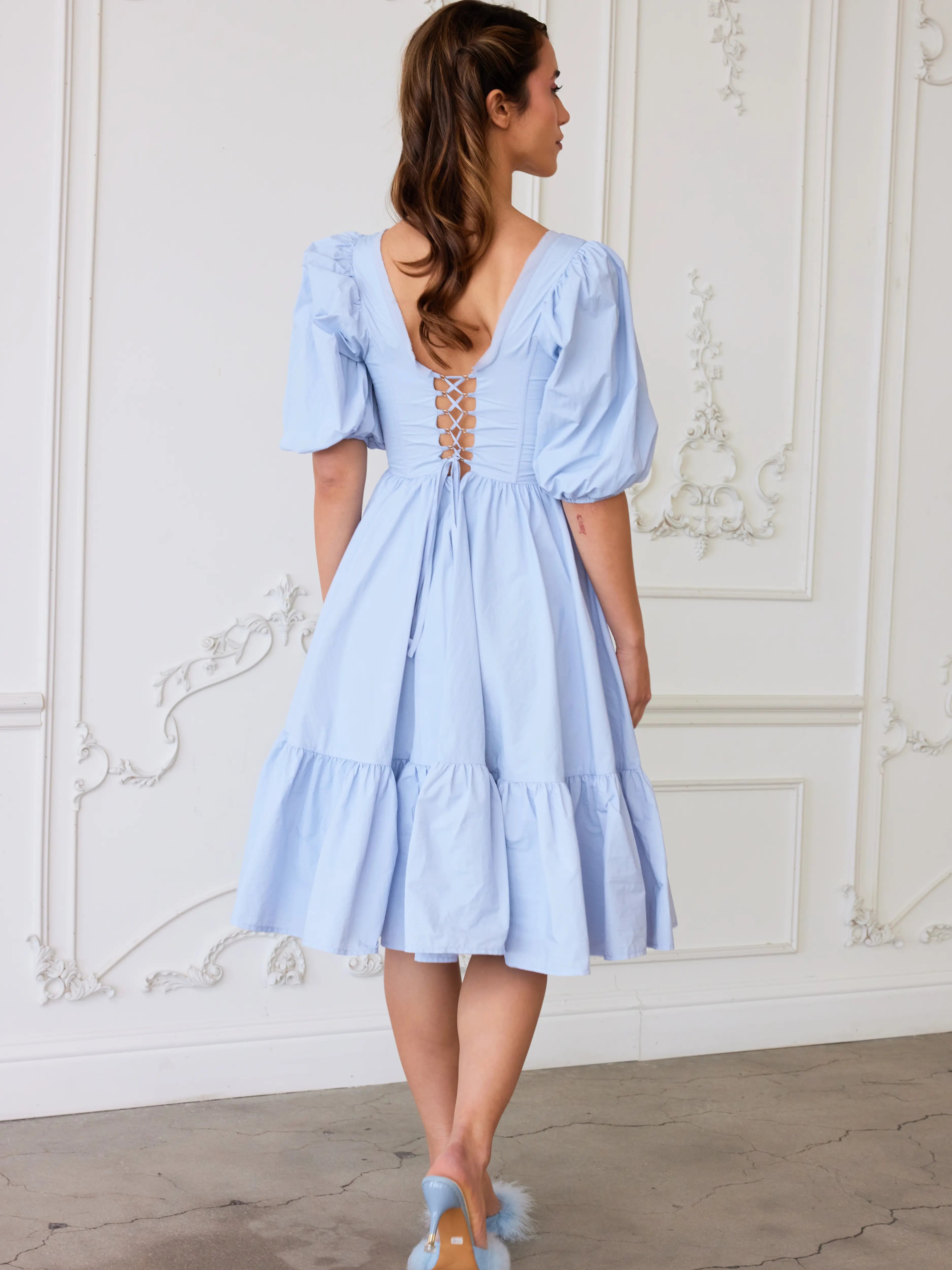 The Alice Blue Josephine Midi Dress, a dress designed with puff sleeves, corset laced back detail, and a ruffled hem.