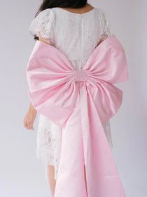 Pink fabric bow on a white lace mini dress featuring the Ballet Pink Grand Bow Sash Belt