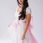 Belladonna Lace Dress styled with pink satin bow sash, highlighting romantic bridal design with lace and high-low silhouette.