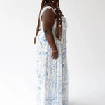 Long white angel dress with delicate blue toile patterns worn against a simple backdrop.