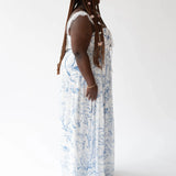 Long white angel dress with delicate blue toile patterns worn against a simple backdrop.