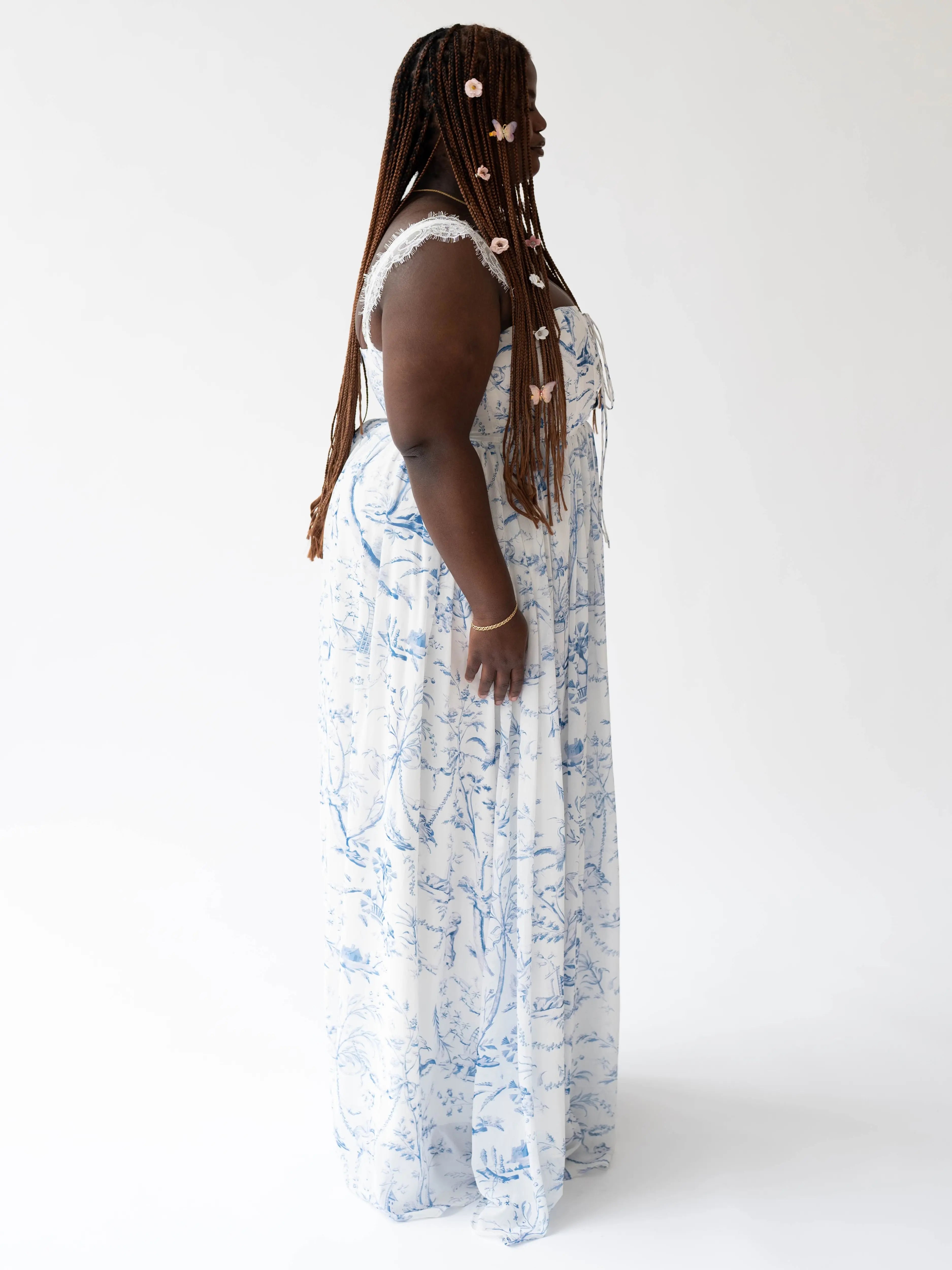 Long white angel dress with delicate blue toile patterns worn against a simple backdrop.