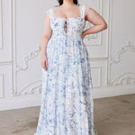 A floor-length white dress with a delicate floral blue toile print. Dress has a corset-style bodice and thin straps with lace details.