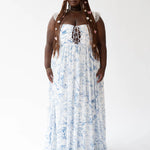 A flowing white maxi dress with delicate blue floral patterns and straps with lace details.