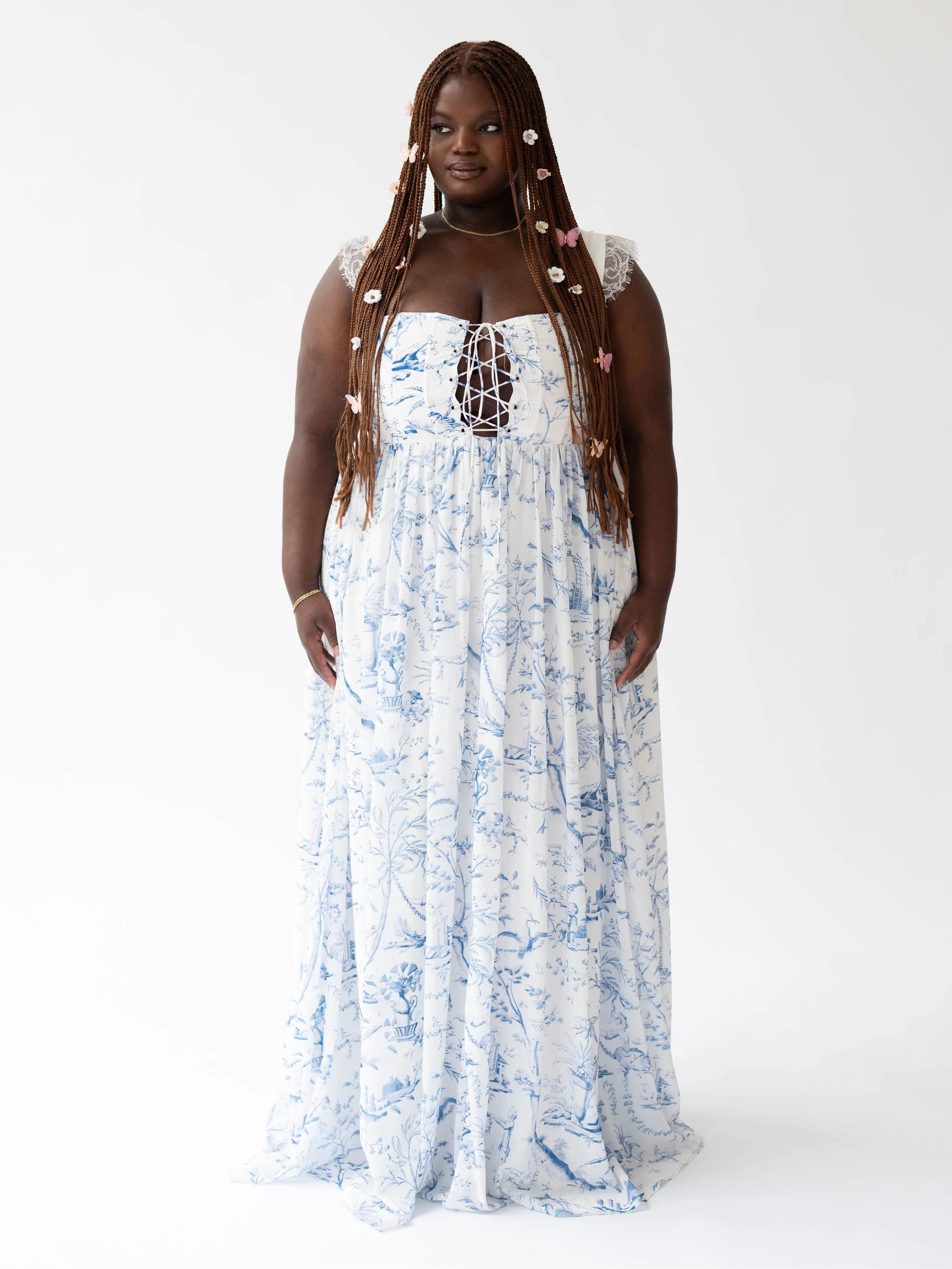 A flowing white maxi dress with delicate blue floral patterns and straps with lace details.