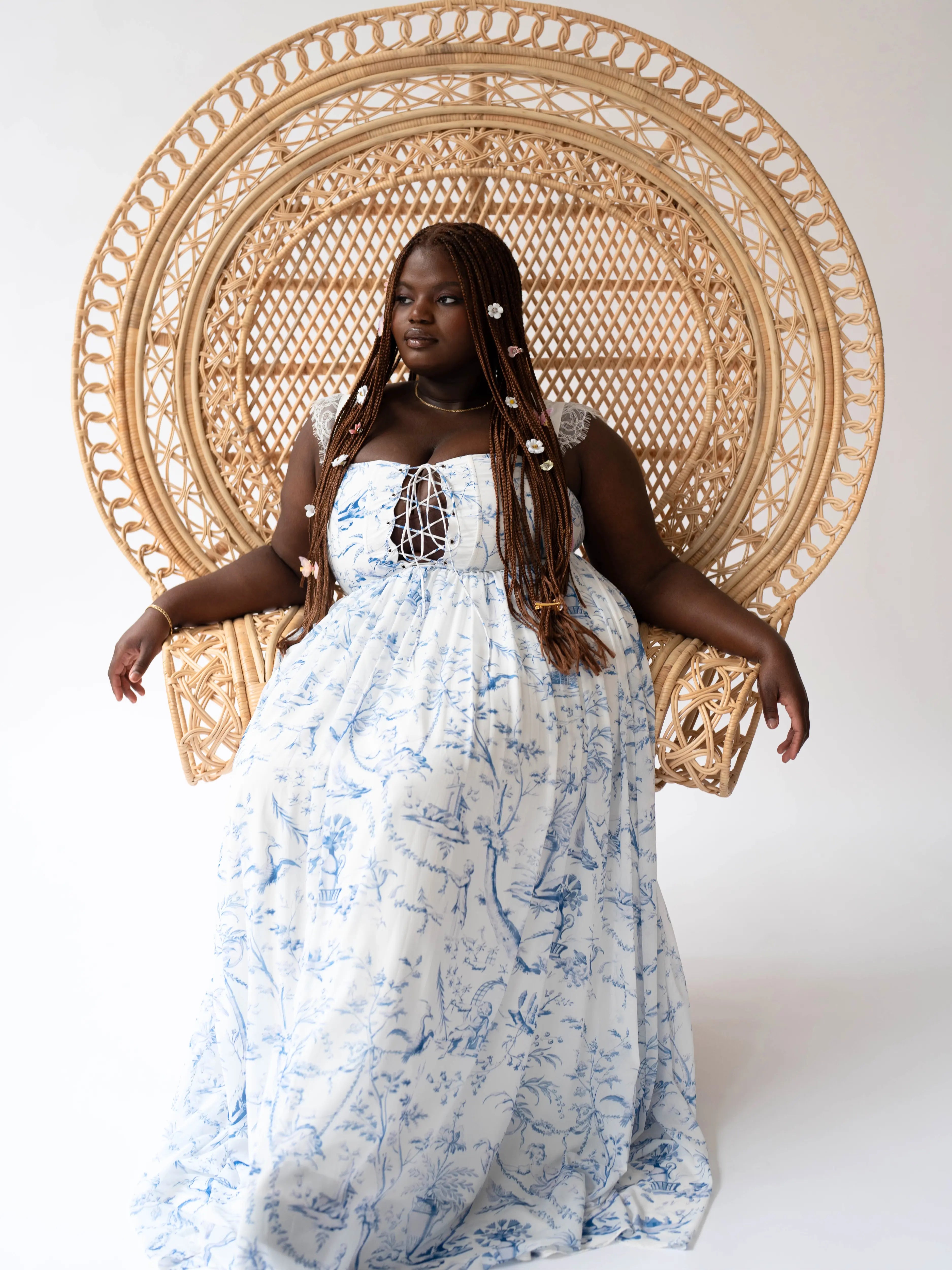 Beautiful white and blue toile printed maxi dress with lace detailed straps against a decorative woven peacock chair.