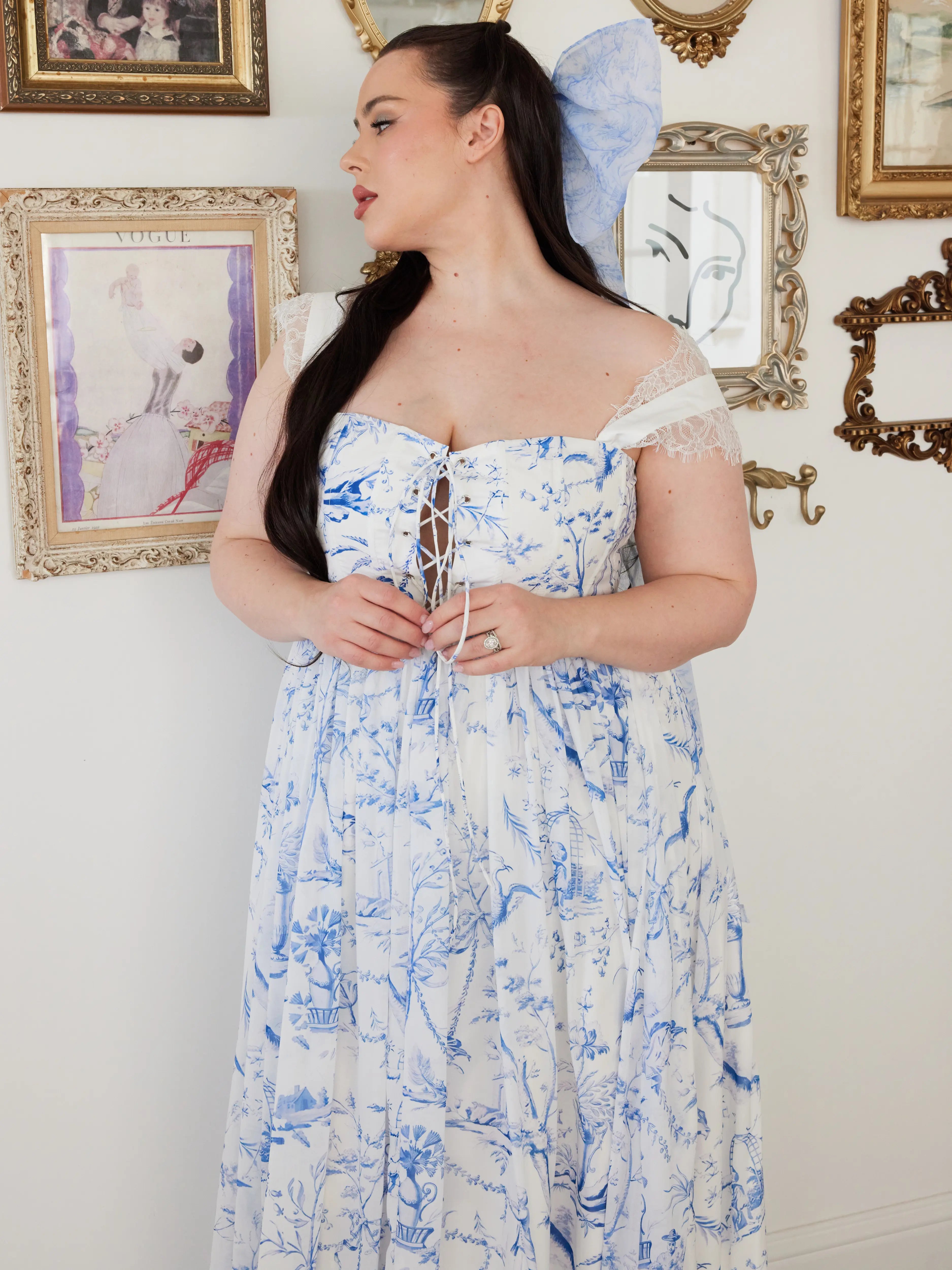 Lace strap, white maxi dress with delicate blue toile print and lace-up corset bodice, paired with an extra large hair bow adorned with the same blue toile print.