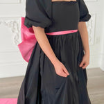 Black dress with puff sleeves and a bright pink sash.