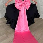 Bright pink satin bow belt with long trailing ribbons attached to a black corset dress.