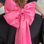 Bright large pink satin bow attached to a black maxi dress.