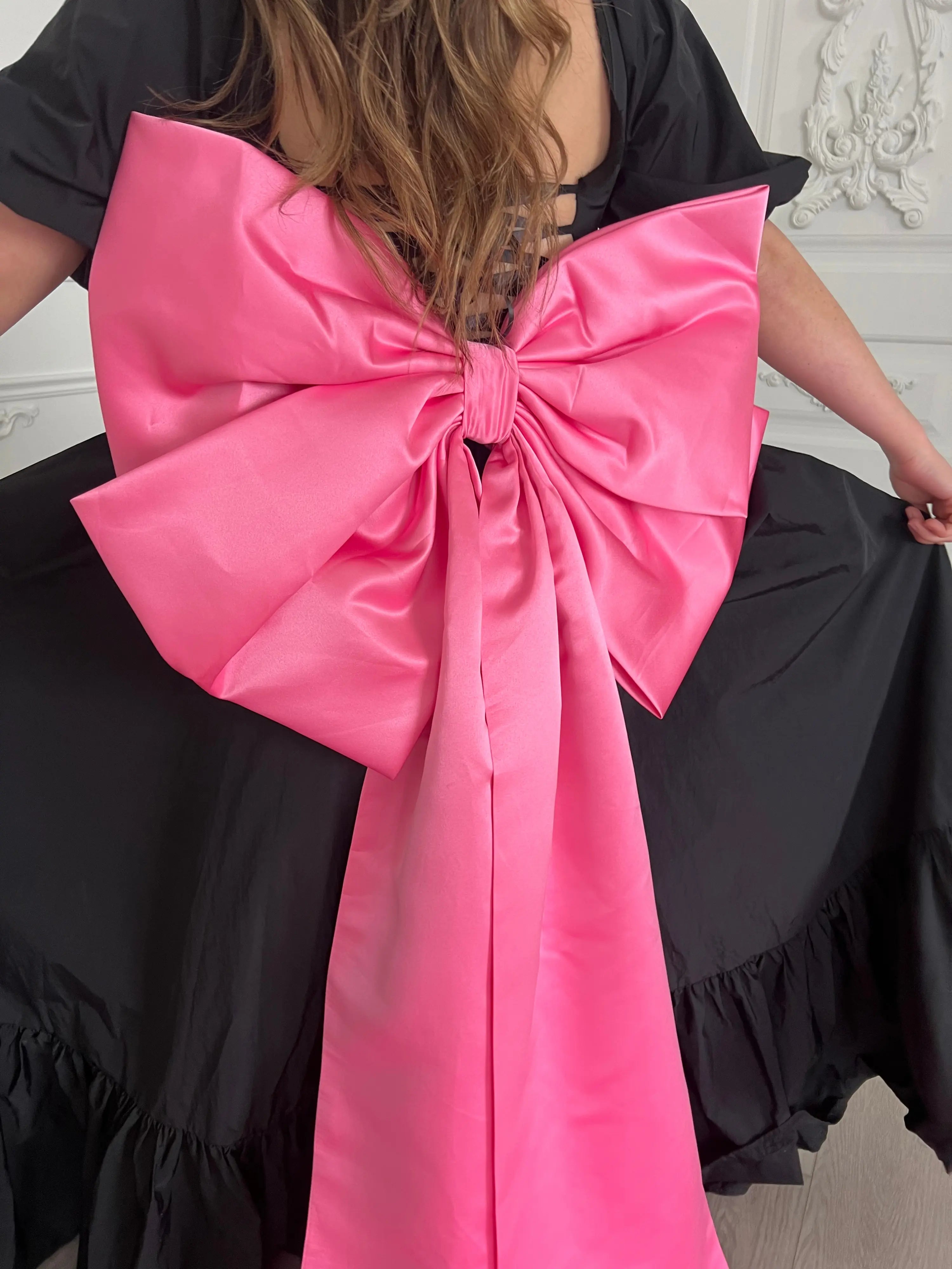 Bright large pink satin bow attached to a black maxi dress.