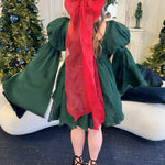 Green mini dress with bell sleeves featuring a giant red Christmas hair bow on a model in a Christmas setting.