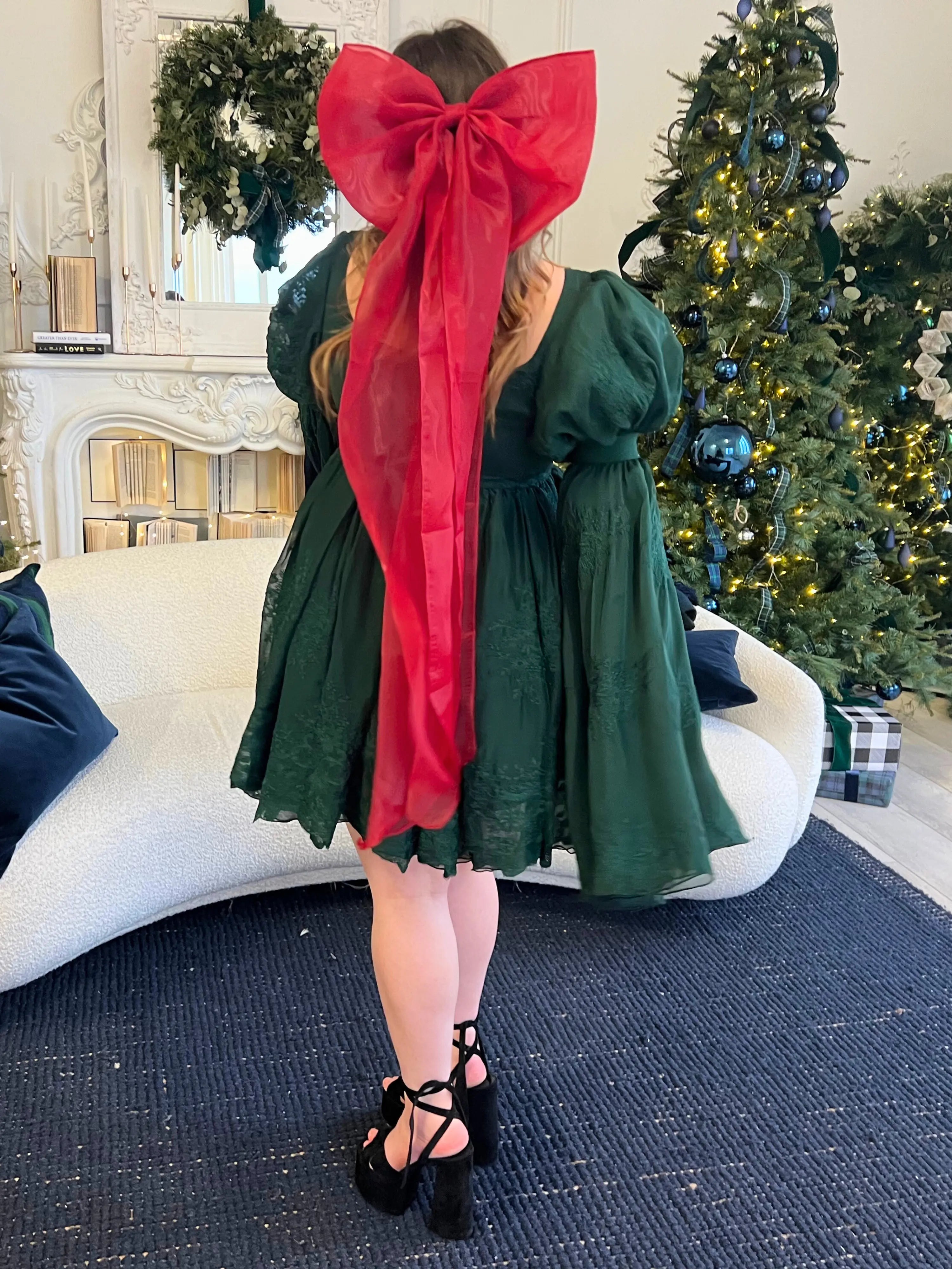 Dark green mini dress featuring a giant holiday red flutter hair bow showcased on someone by Christmas trees.