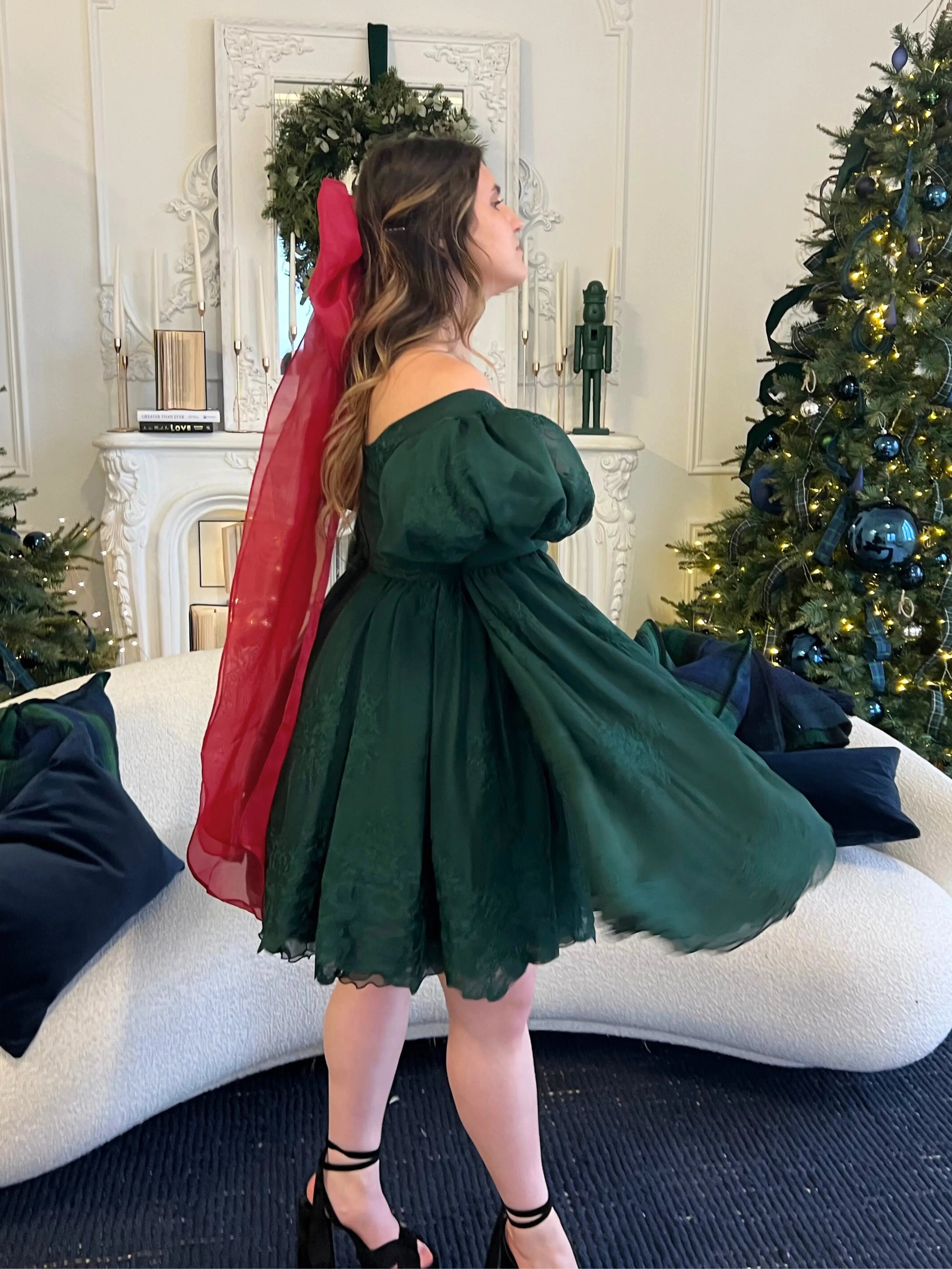 Dark green dress with bell sleeves, flowing skirt, and a giant holiday red flutter bow hair accessory