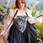 Woman in The Ciela Snow White Shrug Top featuring a black and white floral corset gown with lace trim