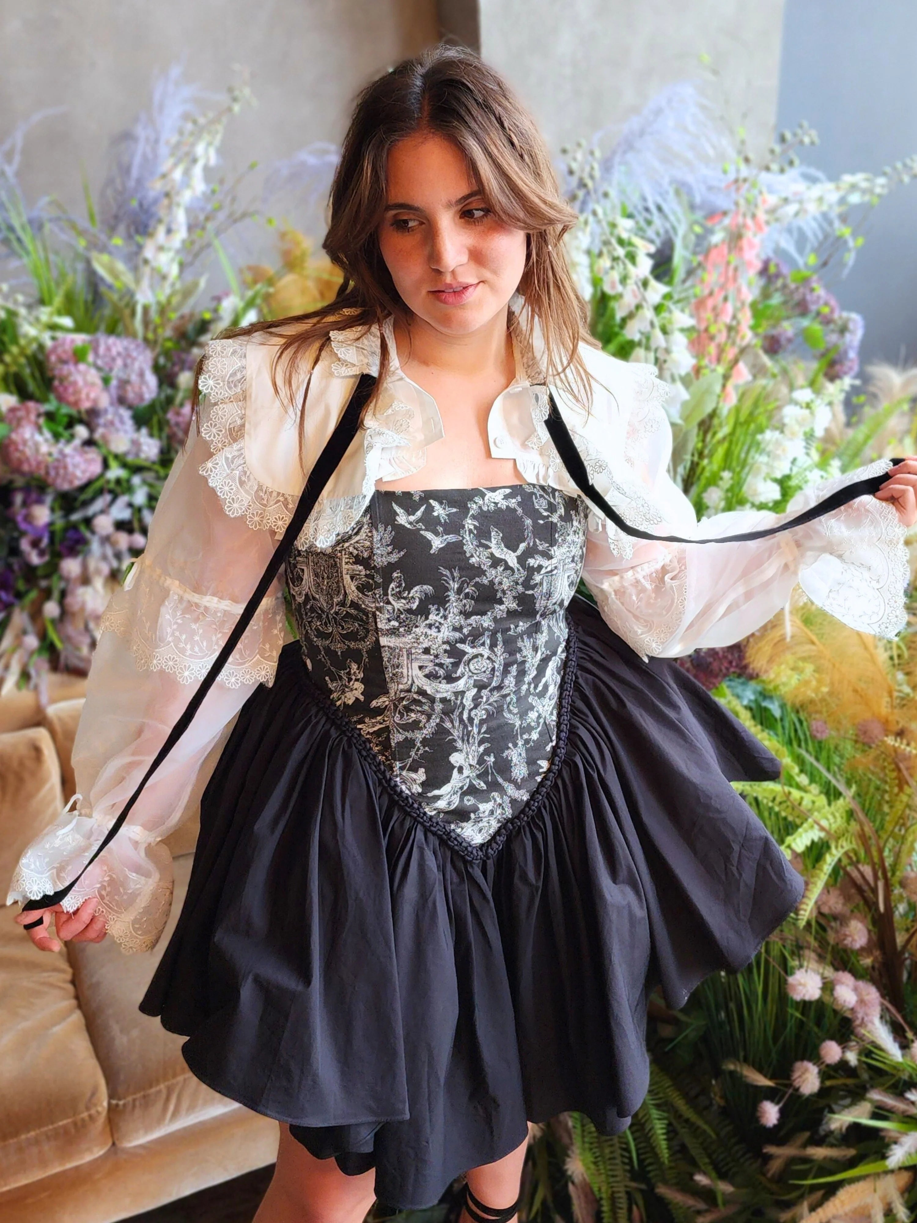 Woman in The Ciela Snow White Shrug Top featuring a black and white floral corset gown with lace trim