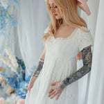 Dauphine Lace Gown with ruffled neckline and puff sleeves, styled with pink bow in a floral wedding backdrop.