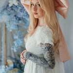 Side profile of model in Dauphine Lace Gown with puff sleeves and pink bow, surrounded by pastel floral wedding decor.