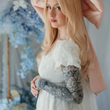 Side profile of model in Dauphine Lace Gown with puff sleeves and pink bow, surrounded by pastel floral wedding decor.