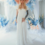 Dauphine Lace Gown bridal maxi dress with puff sleeves and empire waist, styled with oversized pink bow in a floral wedding setting.