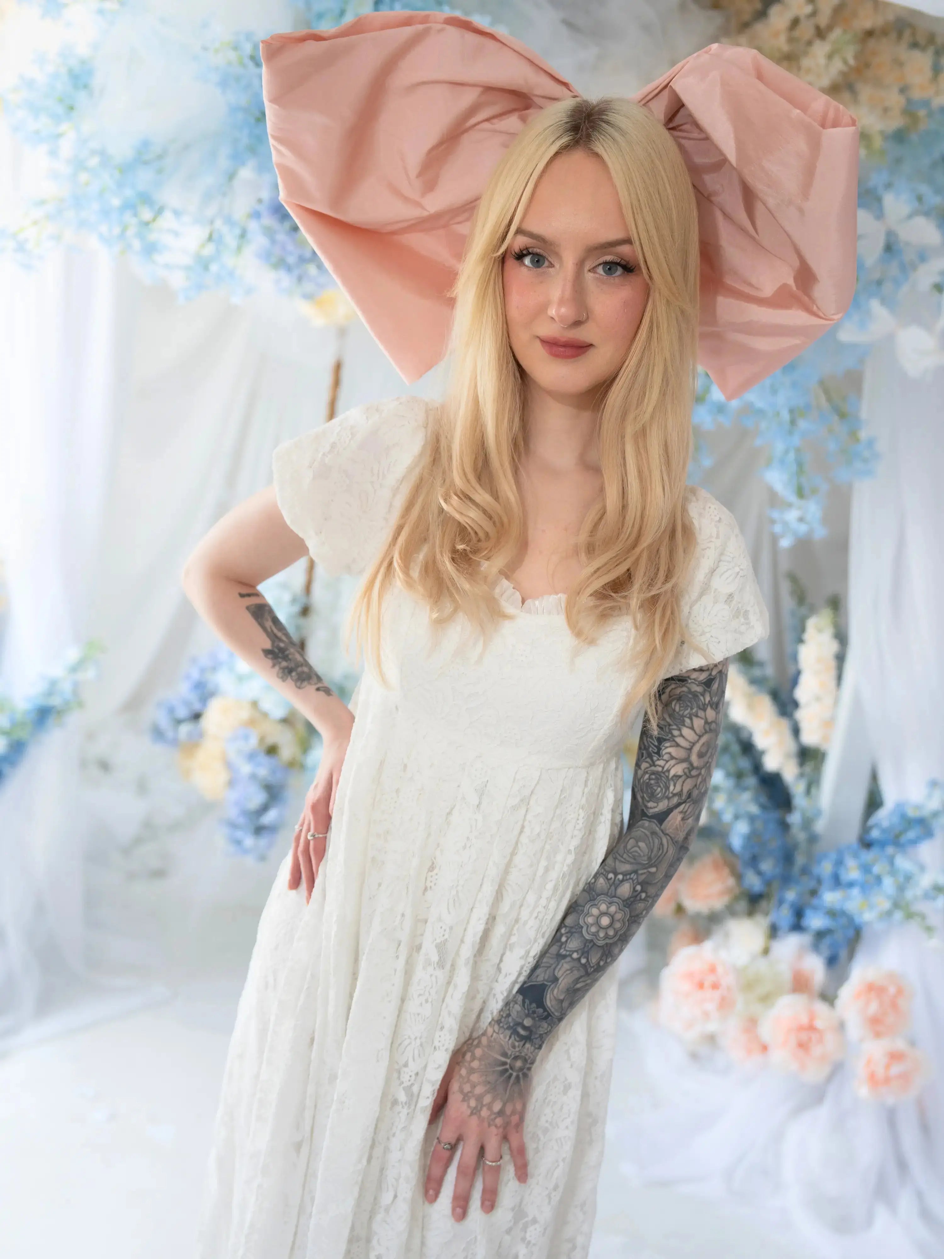 Dauphine Lace Gown styled with oversized pink bow, showcasing romantic lace and empire silhouette in a whimsical wedding setting.