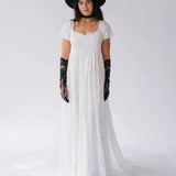Front view of Dauphine Lace Gown featuring square neckline and puff sleeves, styled with black hat and gloves for bridal elegance.