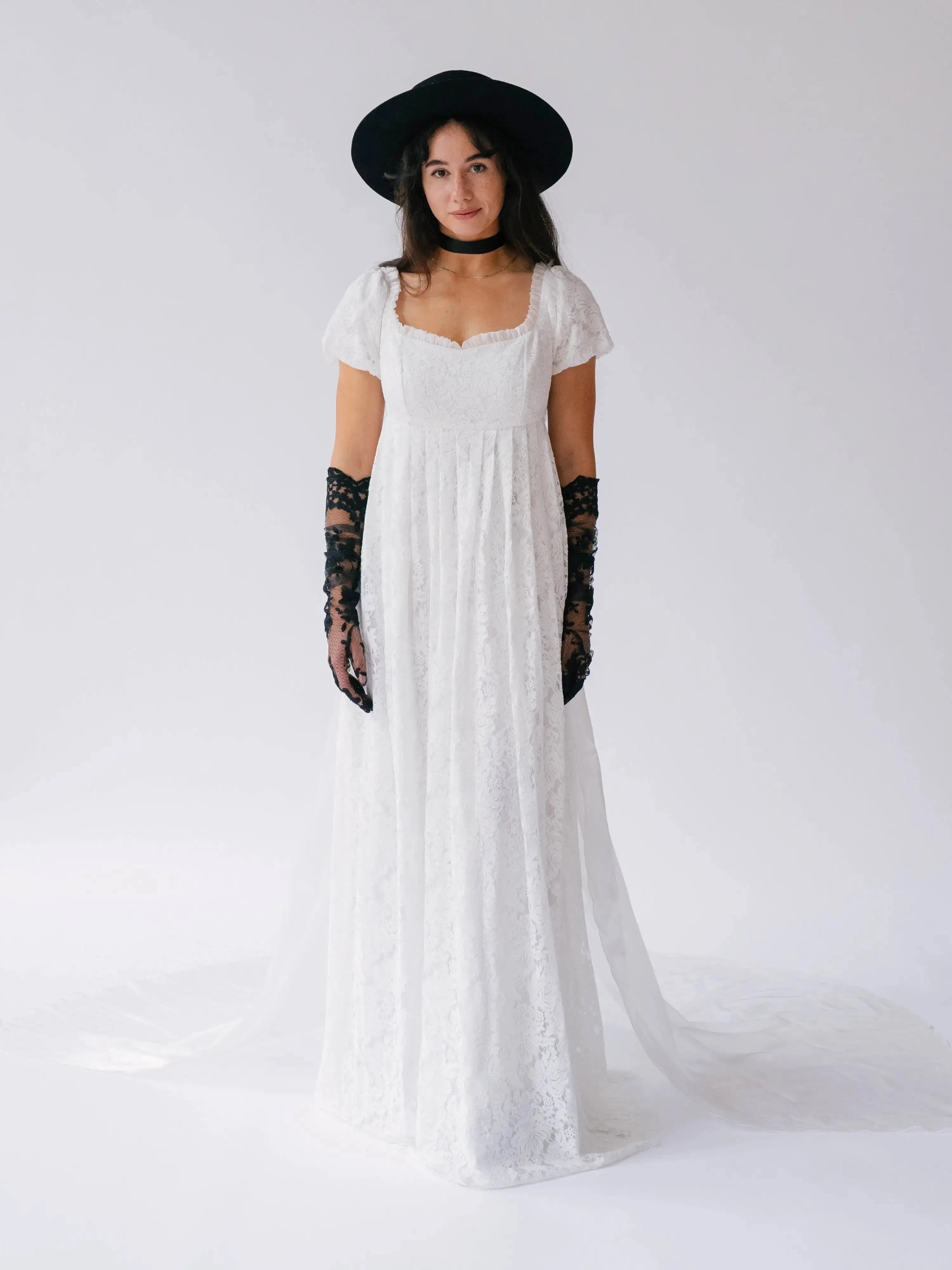 Front view of Dauphine Lace Gown featuring square neckline and puff sleeves, styled with black hat and gloves for bridal elegance.