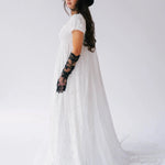 Side view of Dauphine Lace Gown with flowing train and puff sleeves, styled with black hat and lace gloves for a modern bridal look.