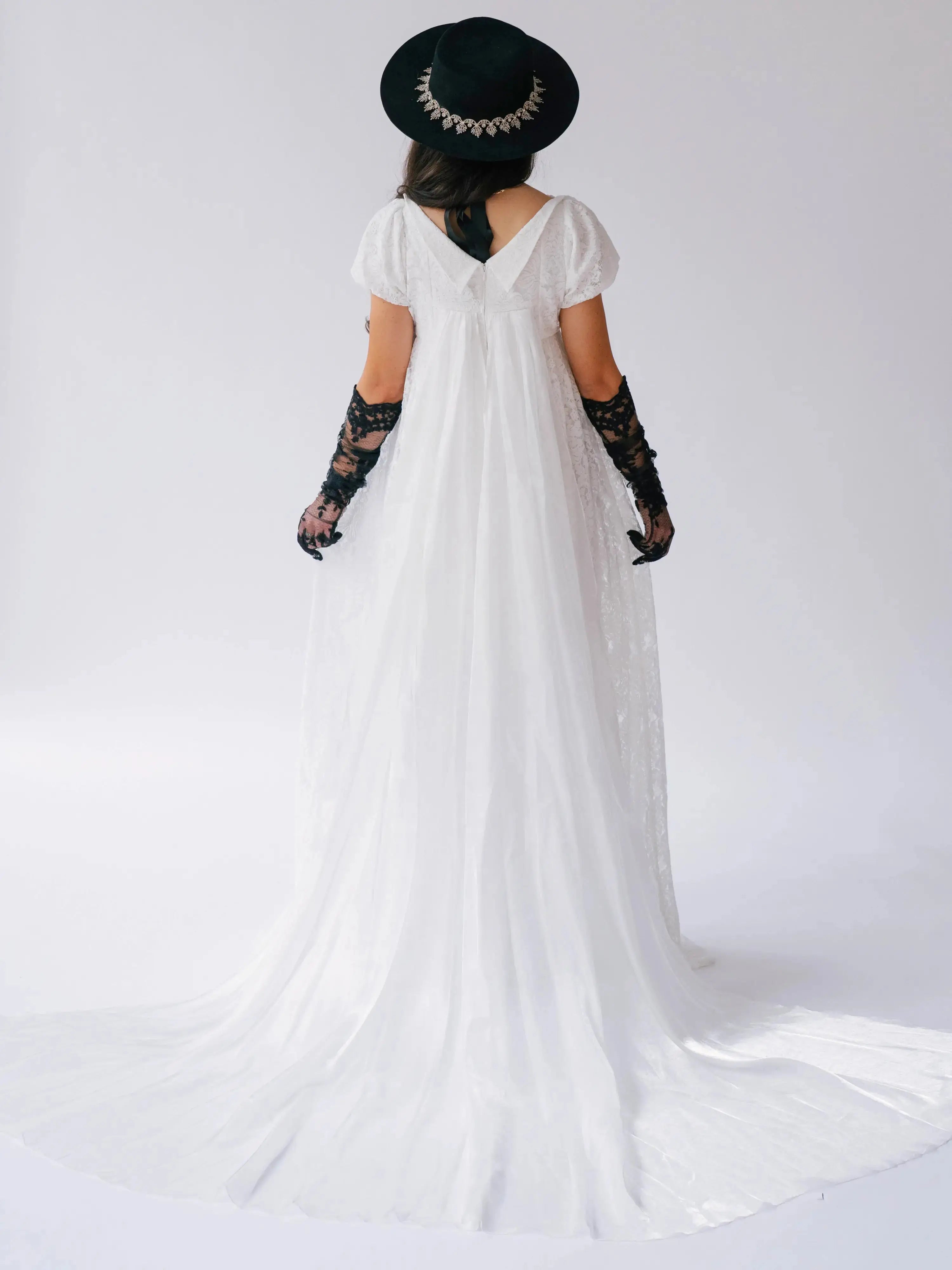 Back view of Dauphine Lace Gown with long train and empire waist, styled with black accessories for a unique wedding dress look.