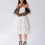 White tiered strapless mini dress with black feathered arm accessories and platform heels.
