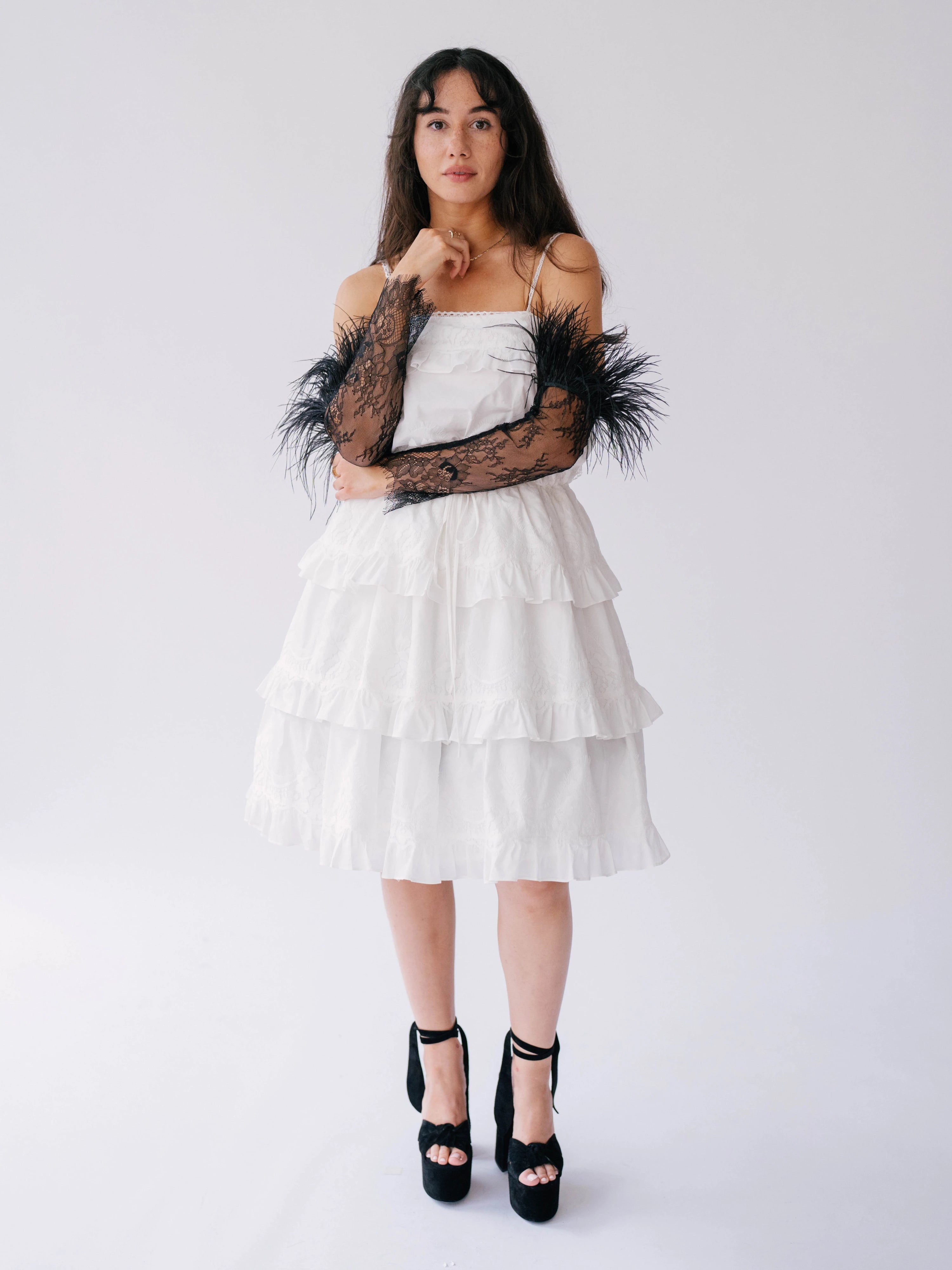 White tiered strapless mini dress with black feathered arm accessories and platform heels.