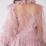 The Eleanor Dusty Pink Lace Blouse is a delicate pink lace blouse with sheer long puff sleeves and is shown close up from the back.