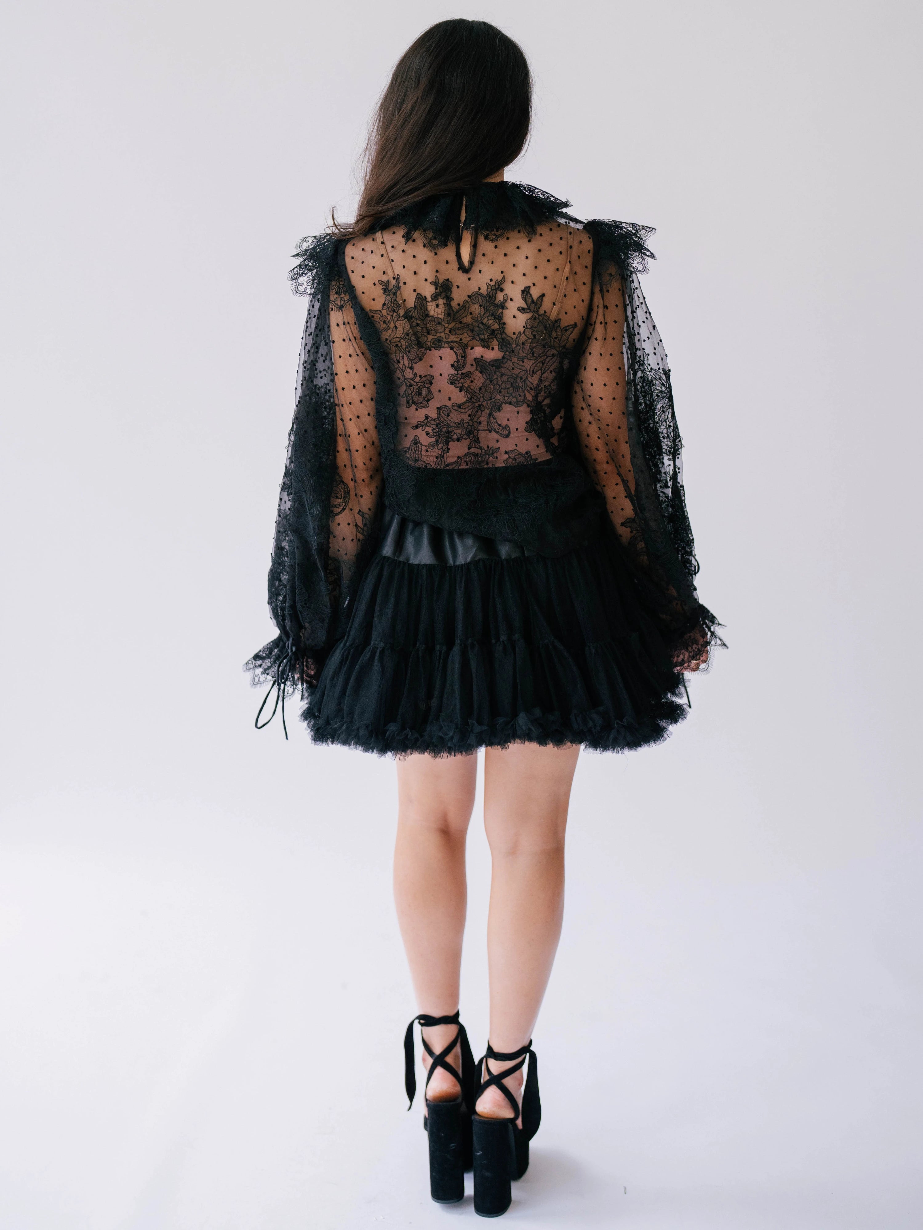 Women's sheer black lace blouse with long puff sleeves shown from the back.