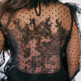 The Eleanor Midnight Black Lace Blouse, a victorian inspired sheer lace blouse with puff sleeves and a delicate floral lace design shown from the back. 
