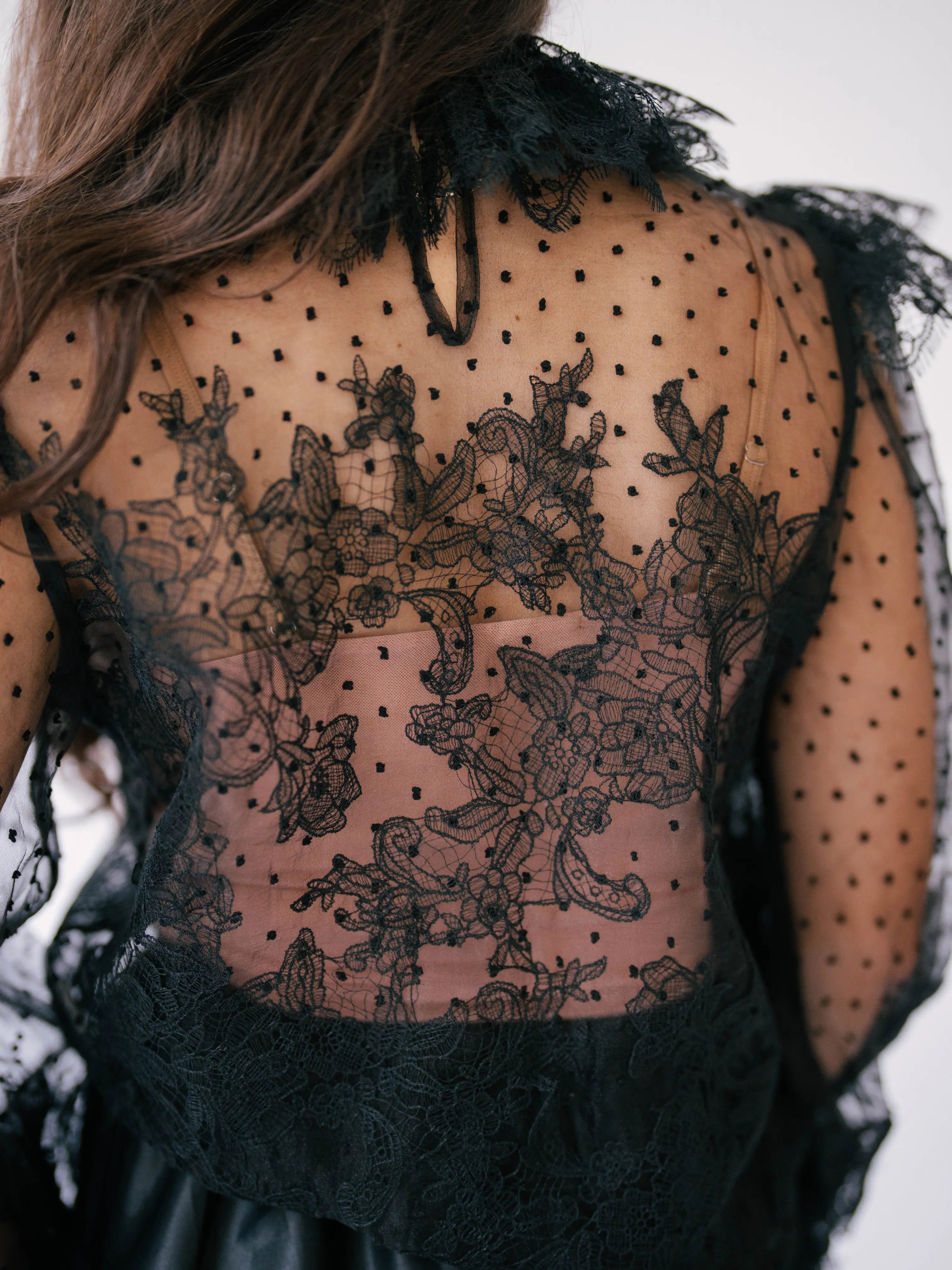 The Eleanor Midnight Black Lace Blouse, a victorian inspired sheer lace blouse with puff sleeves and a delicate floral lace design shown from the back. 