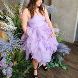 Lavender tulle Eventyr Tulip Dress with ruffled layers, hand cut and hand dyed worn by a woman surrounded by florals.