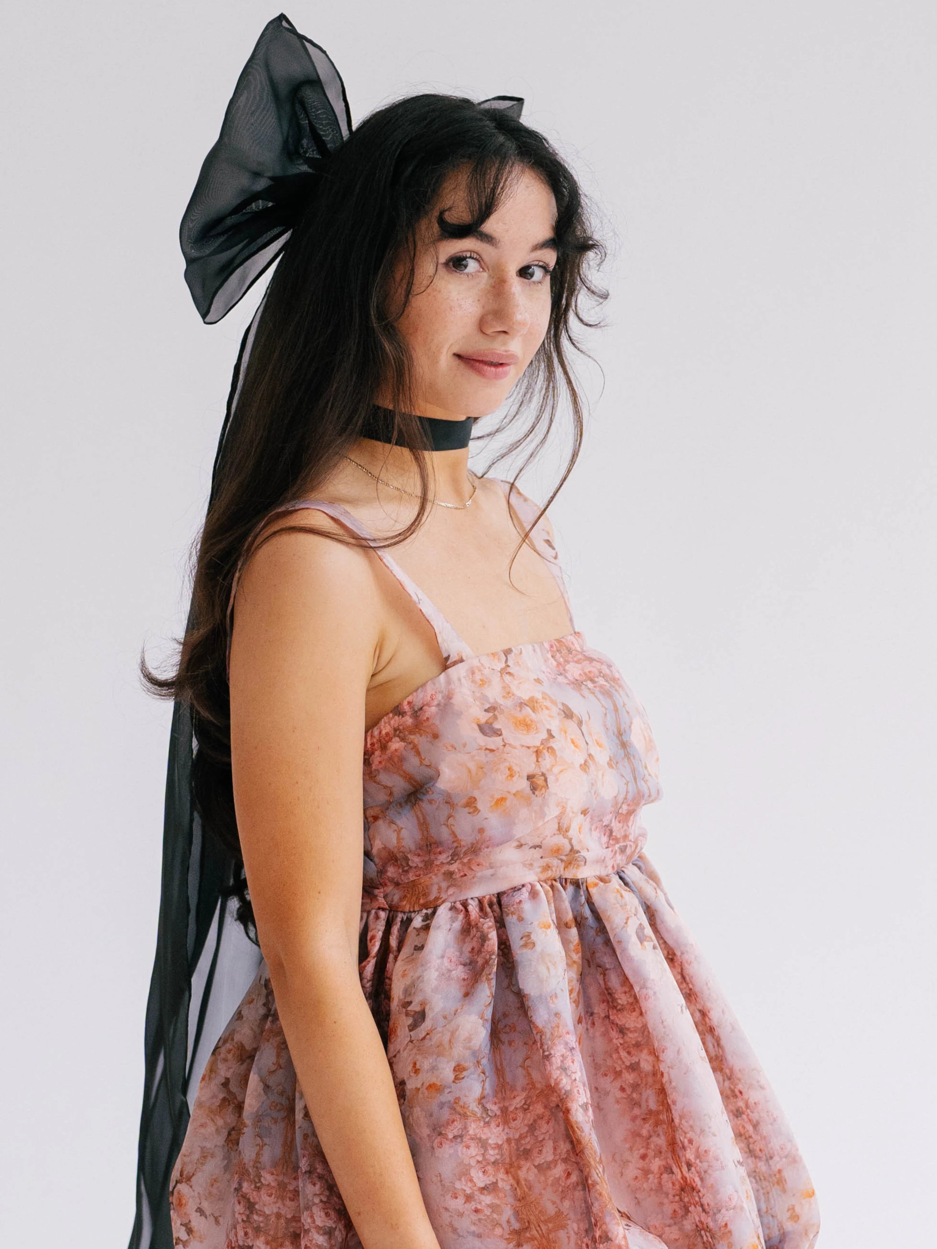 Woman wearing a pink floral gown with spaghetti straps and oversized black hair bow accessory.