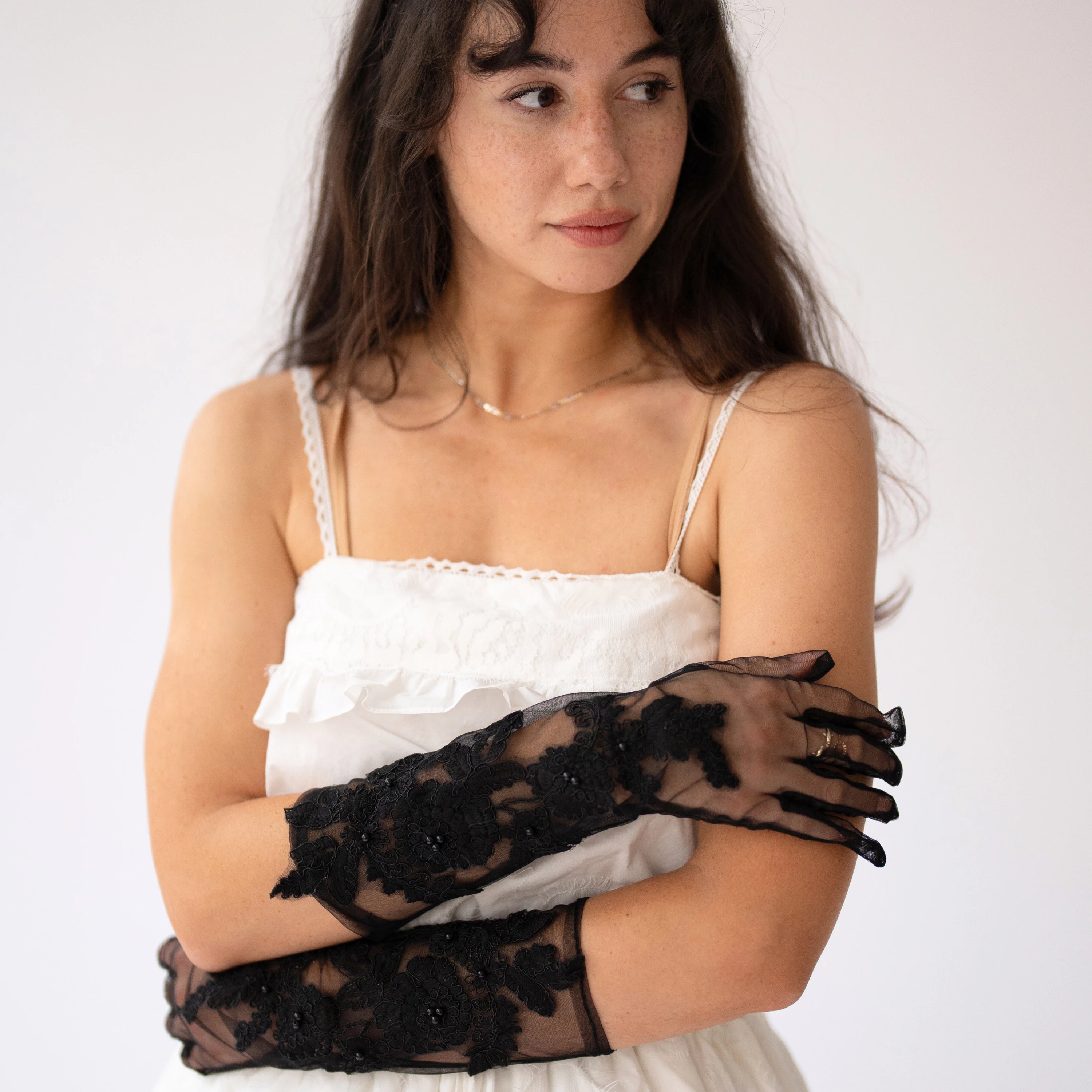 Delicate black lace evening gloves paired with a white ruffled mini dress.