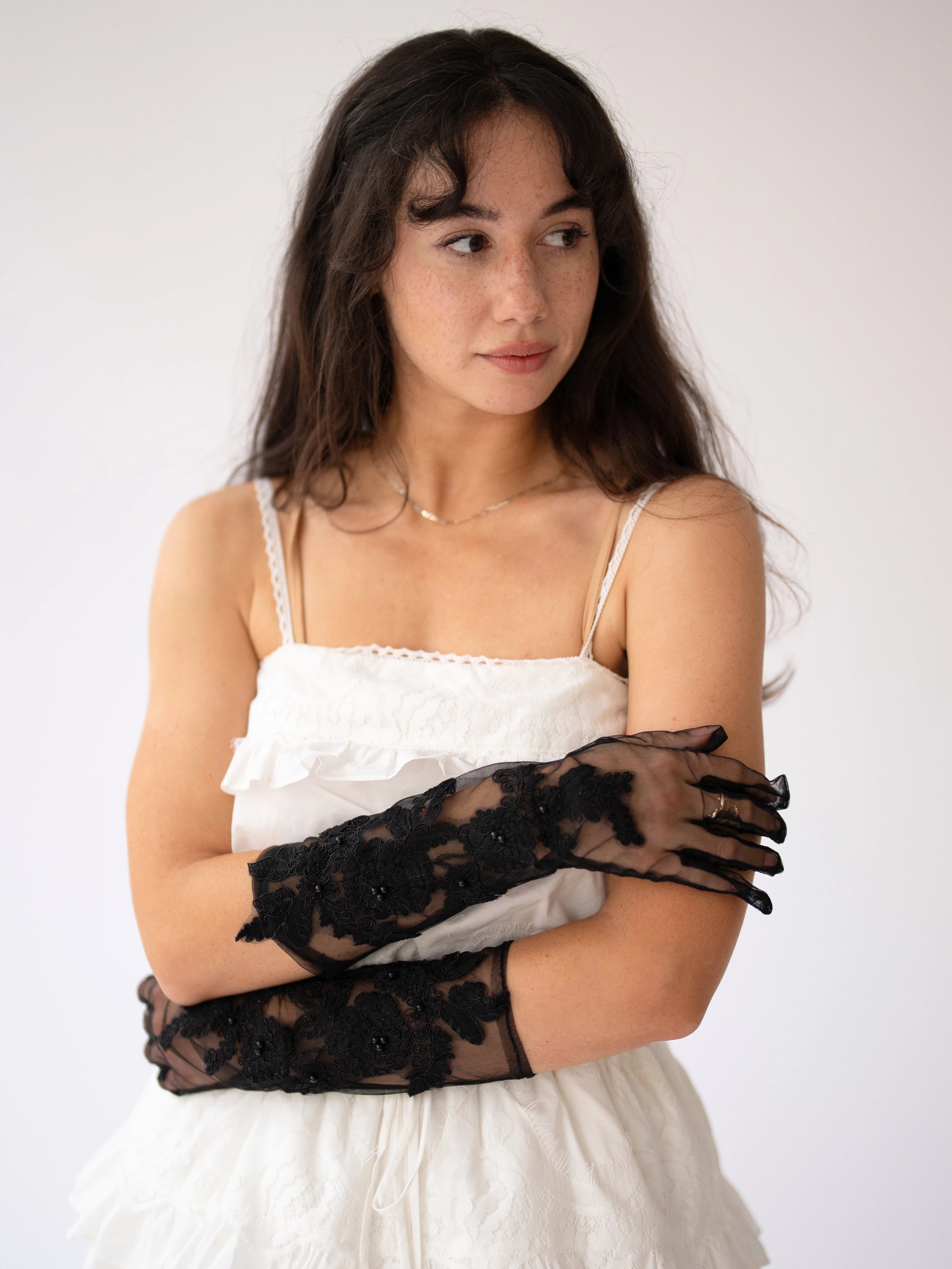 Delicate black lace evening gloves paired with a white ruffled mini dress.