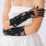Elegant black lace gloves with floral embellishments worn with a white mini dress.