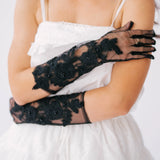 Elegant black lace gloves with floral embellishments worn with a white mini dress.
