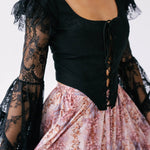 A black lace-sleeved corset top paired with a pink floral bustle skirt.