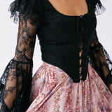 A black lace-sleeved corset top paired with a pink floral bustle skirt.